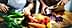 Hands preparing vegetables including lettuce, carrots, tomatoes, and cabbage on a wooden cutting board. - Olive Oil Times