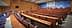 Innenansicht eines Konferenzraums mit Holzsitzen und einer Präsentationsleinwand. - Olive Oil Times