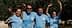 Vier Personen in blauen T-Shirts posieren gemeinsam im Freien unter Olivenbäumen. - Olive Oil Times
