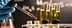 A hand with a blue glove holding a pipette above several test tubes containing yellow liquid. - Olive Oil Times