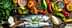 Two whole fish placed on a wooden cutting board surrounded by various vegetables and herbs. - Olive Oil Times