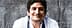 Smiling chef with curly hair wearing a white chef jacket and a gray apron. - Olive Oil Times