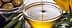 A glass bowl filled with olive oil, with olives and olive leaves nearby. - Olive Oil Times