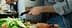 A person stirring food in a frying pan while preparing ingredients on a kitchen countertop. - Olive Oil Times