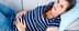 Pregnant woman in a striped shirt lying on a couch with a pained expression, holding her stomach. - Olive Oil Times