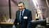 A man in a dark suit and tie standing at a podium during a conference presentation. - Olive Oil Times