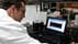 A scientist in a lab coat examining data displayed on a laptop screen in a laboratory setting. - Olive Oil Times
