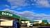Bâtiment d'entrepôt Dcoop avec deux camions garés devant sous un ciel bleu. - Olive Oil Times