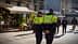 Two police officers in green and black uniforms walking in an urban area with a flower shop in the background. - Olive Oil Times