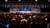 A large audience gathered in a convention center for a conference event with screens displaying presentations. - Olive Oil Times