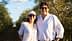 Un homme et une femme souriant debout dans une oliveraie sous un ciel clair. - Olive Oil Times