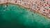 Aerial view of a crowded beach with swimmers and colorful umbrellas along the shoreline. - Olive Oil Times
