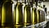Row of glass bottles filled with olive oil on a production line in a factory setting. - Olive Oil Times
