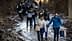 A group of people walking along a muddy path in a wooded area, some carrying bags. - Olive Oil Times