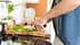 A person using a knife to chop green vegetables on a wooden cutting board in a kitchen. - Olive Oil Times