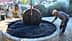 Man operating a traditional olive press with a horse in the background and olives in a stone basin. - Olive Oil Times
