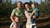 Une famille de quatre personnes posant ensemble dans une oliveraie, avec deux enfants et deux adultes souriant à la caméra. - Olive Oil Times