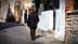 Um homem idoso caminhando por uma rua de paralelepípedos ladeada por prédios e vegetação. - Olive Oil Times