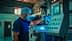 A worker in a blue shirt and hairnet operating a control panel in an industrial environment. - Olive Oil Times