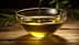 Una ciotola di vetro trasparente piena di olio d'oliva, con rami d'ulivo posizionati lì vicino su una superficie di legno. - Olive Oil Times