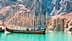 Un bateau de pêche coloré ancré dans une eau turquoise avec de grands arbres nus en arrière-plan. - Olive Oil Times