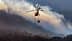 Helicóptero voando sobre uma área montanhosa com um balde de água suspenso abaixo dele. - Olive Oil Times