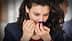 Woman with curly hair smelling from a blue glass container in a neutral setting. - Olive Oil Times