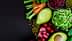 Eine Auswahl an frischem Gemüse, darunter Karotten, Sellerie und Avocado, angeordnet auf einer dunklen Oberfläche. - Olive Oil Times