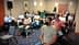 Group of people seated in a meeting room, some wearing masks, listening to a speaker. - Olive Oil Times