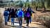 A group of people walking along a dirt path in an olive grove, wearing winter clothing and backpacks. - Olive Oil Times