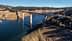 Un ponte che attraversa uno specchio d'acqua con pilastri di sostegno e paesaggio circostante. - Olive Oil Times