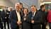 Three individuals standing together, each holding a glass, in a gathering or event setting. - Olive Oil Times