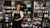 Una mujer con delantal se encuentra junto a una exhibición de productos decorativos en estantes. Olive Oil Times