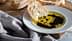 Fatia de pão mergulhada em azeite de oliva com vinagre balsâmico em um prato branco. Olive Oil Times
