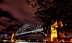 El Puente del Puerto de Sídney iluminado por la noche con un cielo despejado y nubes al fondo. - Olive Oil Times