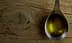 Cuchara de metal llena de aceite de oliva que reposa sobre una superficie de madera texturizada. - Olive Oil Times
