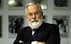A man with a white beard wearing glasses and a suit, standing with arms crossed. - Olive Oil Times