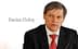 Ο Dacian Cioloș, ένας άντρας με κοστούμι με κόκκινη γραβάτα, καθισμένος και δείχνει σοβαρός. - Olive Oil Times