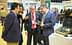 Four individuals engaged in conversation while examining olive oil products at an event. - Olive Oil Times