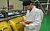 Man in a lab coat taking notes while observing yellow machinery in a facility. - Olive Oil Times
