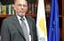 A man in a gray suit standing next to a flag of Cyprus and the European Union flag. - Olive Oil Times