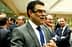 A man in a gray suit with a blue tie speaking in a group setting with other men in suits. - Olive Oil Times