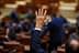 Uma mão levantada em um ambiente formal, possivelmente durante uma votação em uma assembleia legislativa. - Olive Oil Times