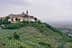 A hilltop village with buildings and a church tower, surrounded by olive trees and rolling hills. - Olive Oil Times