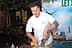 Chef in a white uniform mixing ingredients in a bowl at an outdoor event with a backdrop. - Olive Oil Times