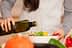 Individual pouring olive oil from a bottle into a salad bowl filled with vegetables. - Olive Oil Times