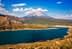 Montagne enneigée avec un ciel bleu clair au-dessus d'un grand lac entouré de collines. - Olive Oil Times