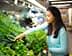 食料品店の陳列棚から新鮮な野菜を選んでいる長い黒髪の女性。 - Olive Oil Times