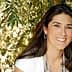 Woman with long dark hair smiling while wearing a white top and earrings. - Olive Oil Times