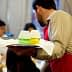 Waiter in a red apron holding a tray with two glasses of colored drinks at a dining event. - Olive Oil Times